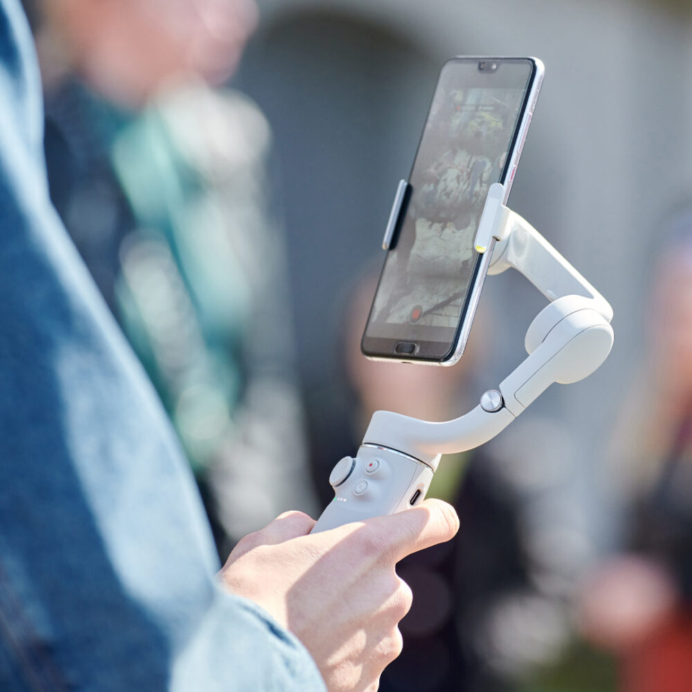 Blogger filming outdoor event on smartphone with gimbal stabilizer, video blogging for new followers. Video shooting content for social media networks, vlog video making